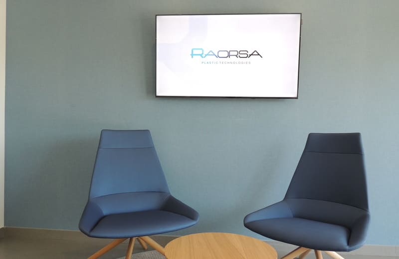 Dentro de las oficinas de Raorsa Maquinaria, dos sillas con TV en el fondo, en pantalla el logo de Raorsa